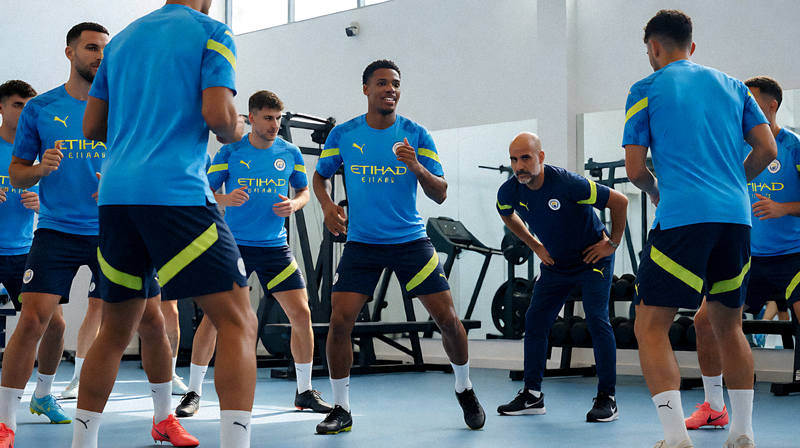 曼城球队在新援加入后进行首次集体训练，新球员身穿蓝色训练服融入团队，瓜迪奥拉在场边观察指导